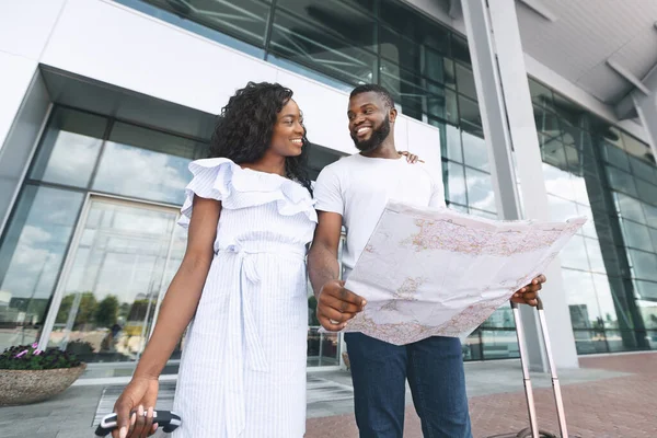 Feliz pareja africana saliendo del aeropuerto con el mapa en las manos — Foto de Stock