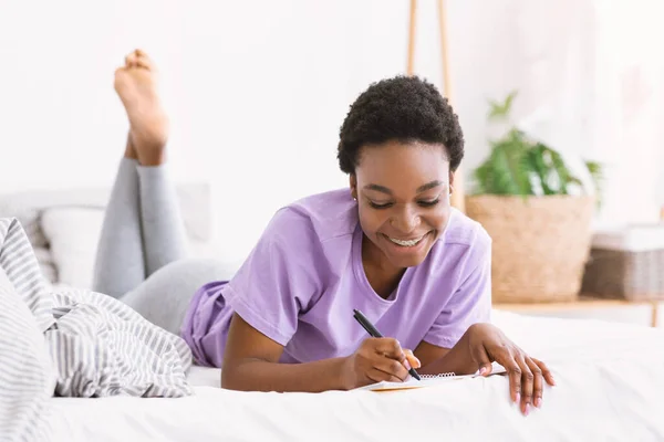 Keep a personal diary. Girl lies on bed and writes in notebook — Stock Photo, Image