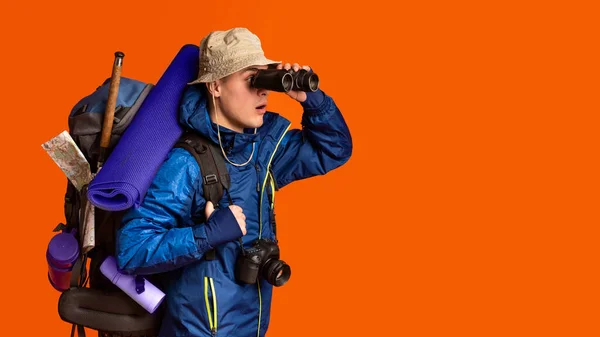 Backpacker pomocí dalekohledu, při pohledu na volné místo přes oranžové pozadí — Stock fotografie