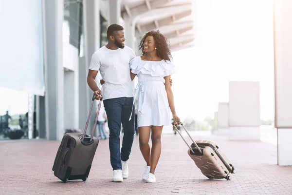 Viajar juntos. Pareja negra feliz caminando con maletas cerca del edificio del aeropuerto —  Fotos de Stock