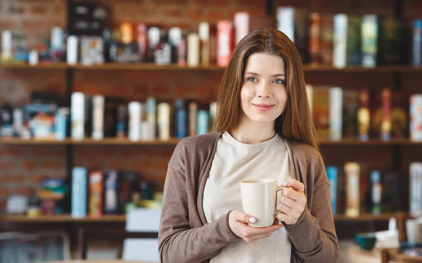 Portret van een vrouw in een cafetaria die hete cappuccino drinkt en naar de camera kijkt — Stockfoto