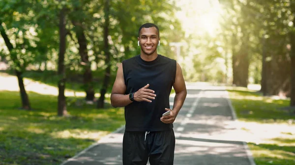 Millennial Africano jogger americano com smartphone ouvindo música durante seu treinamento no parque — Fotografia de Stock