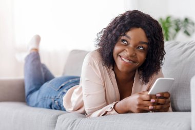 Rüyalarımın siyahi kızı kanepede uzanıyor ve evdeki akıllı telefondan mesajlaşıyor.