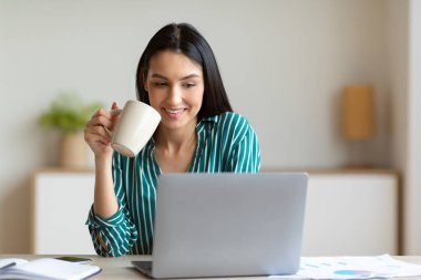 İş kadını laptopta çalışıyor. İş yerinde kahve içiyor.