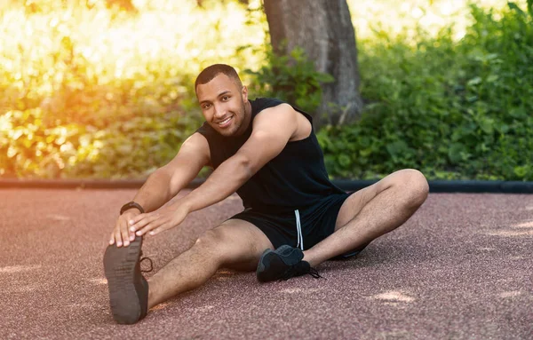 Attraktiver schwarzer Kerl streckt seine Beine auf Asphaltstraße im Park — Stockfoto