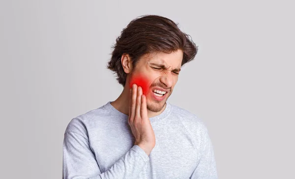 Schmerz ertragen. Trauriger Mann leidet unter Schmerzen in den Zähnen und drückt Hand auf roten Fleck — Stockfoto