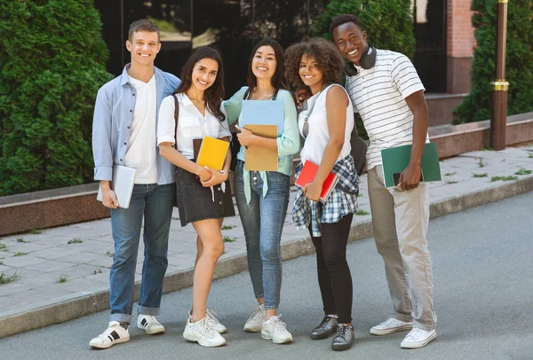 Multiethnic group of students standing outdoors in school campus with workbooks — Stock Photo, Image