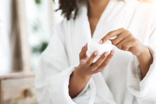 Mujer negra irreconocible sosteniendo tarro con crema natural orgánica en sus manos —  Fotos de Stock