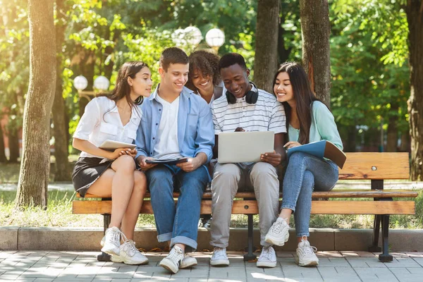 Amigos universitários multiétnicos descansando no campus ao ar livre, usando laptop juntos — Fotografia de Stock