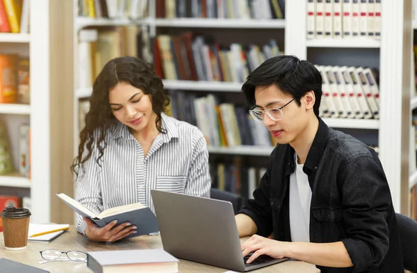 Két mosolygó multikulturális diák tanul az egyetemi könyvtárban. — Stock Fotó