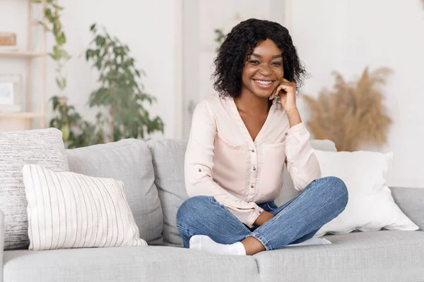 Комфорт дома. Счастливая африканская девушка позирует на диване в гостиной — стоковое фото