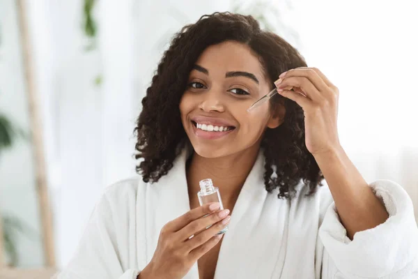 Sorridente afro donna applicazione idratante viso siero sulla sua bella pelle — Foto Stock