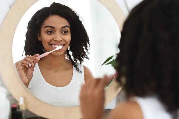 Cuidados Odontológicos diários. Sorrindo Africano Mulher escovar os dentes perto do espelho no banheiro — Fotografia de Stock