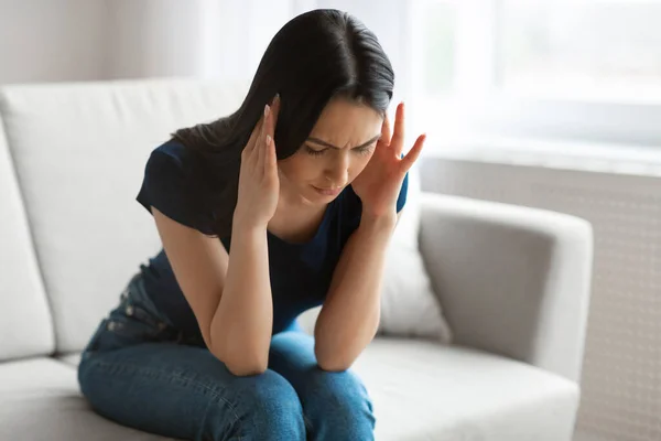 Frau leidet unter Kopfschmerzen, wenn sie auf Sofa im Haus sitzt — Stockfoto