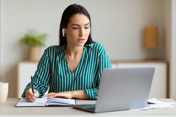 Mujer en el ordenador portátil tomando notas combinando trabajo y estudio en interiores — Foto de Stock