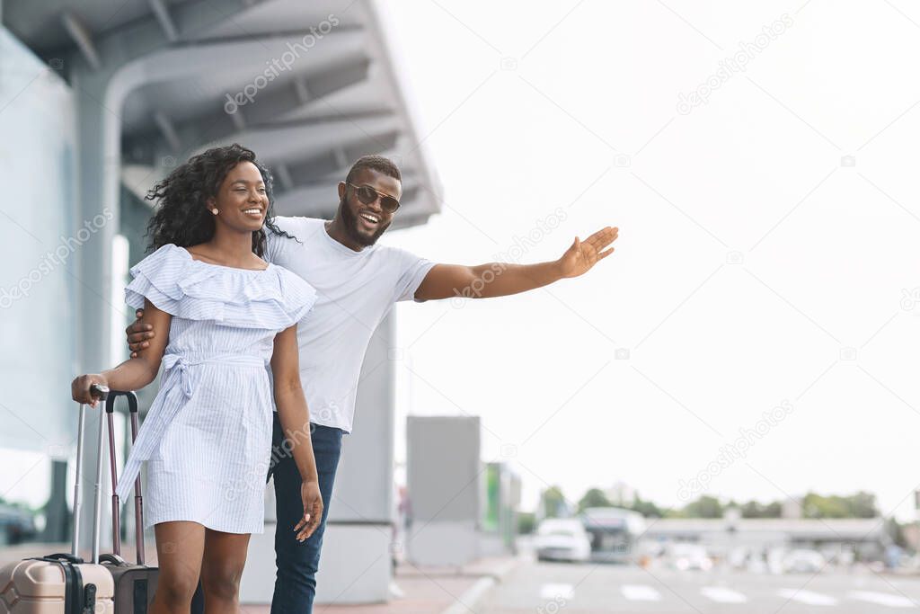 Catching cab. Happy black couple standing at airport parking, calling taxi