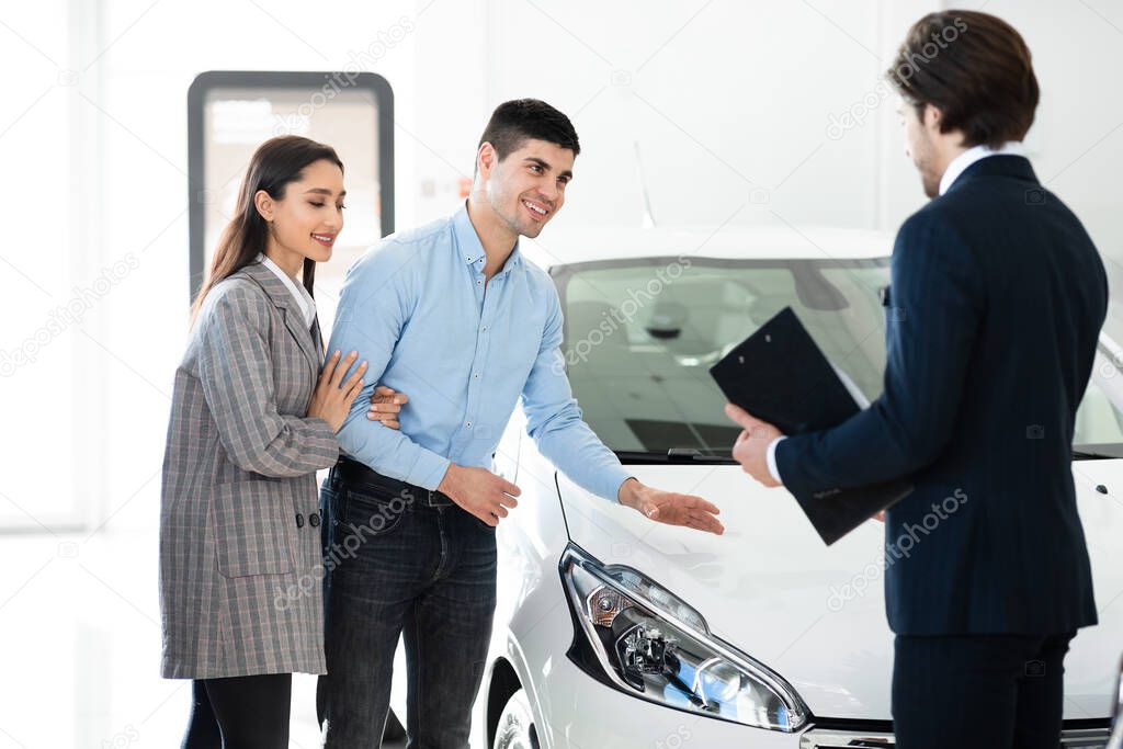 Salesman Offering New Car Standing In Auto Showroom