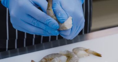 Eldivenli şef mutfakta taze karides soyuyor.