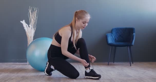 Joven chica en forma atando cordones, preparándose para el entrenamiento en casa — Vídeos de Stock