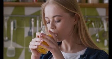 Neşeli kız mutfakta taze portakal suyu içiyor.