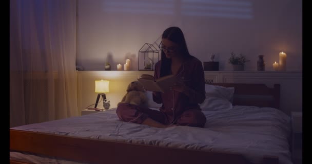 Joven mujer inteligente leyendo libro en la cama tarde — Vídeo de stock