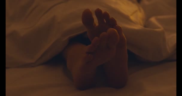 Primo piano di piedi femminili sotto coperta, ragazza che dorme a letto — Video Stock