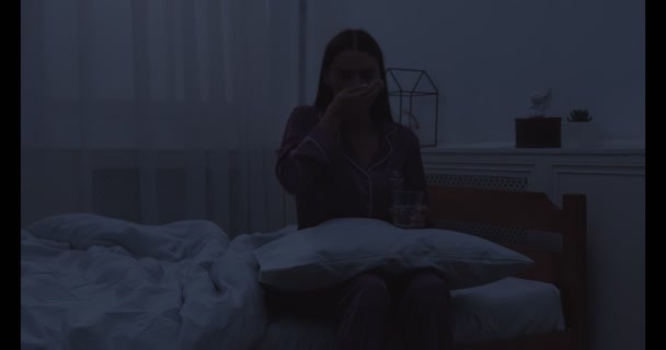 Mladá žena sedí na posteli a bere prášky na spaní v ložnici — Stock video