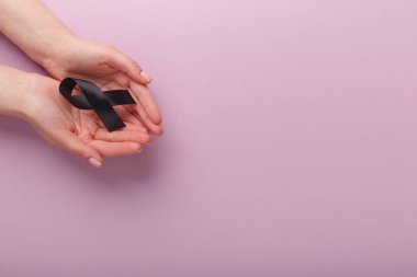 Pembe arka planda avuçlarda siyah farkındalık kurdelesi