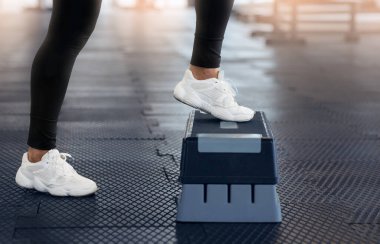 Spor ayakkabılı genç bir kadının spor salonunda spor platformuyla egzersiz yapması, yakın çekim.