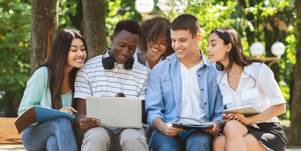 Lista de estudiantes aceptados. Felices amigos adolescentes interraciales utilizando el ordenador portátil al aire libre — Foto de Stock