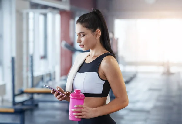 Millennial-Frau mit Handy und Flasche Wasser oder Proteinshake im Fitnessstudio — Stockfoto
