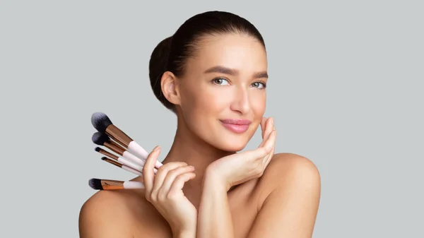 Smiling caucasian young woman holding her makeup brushes — Stock Photo, Image