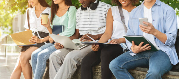 Students preparing for lessons, sitting in campus with books and devices