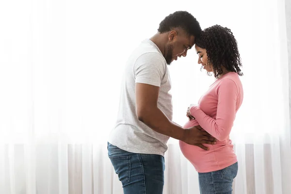 Husband and pregnant wife cuddling next to window at home — Stock Photo, Image