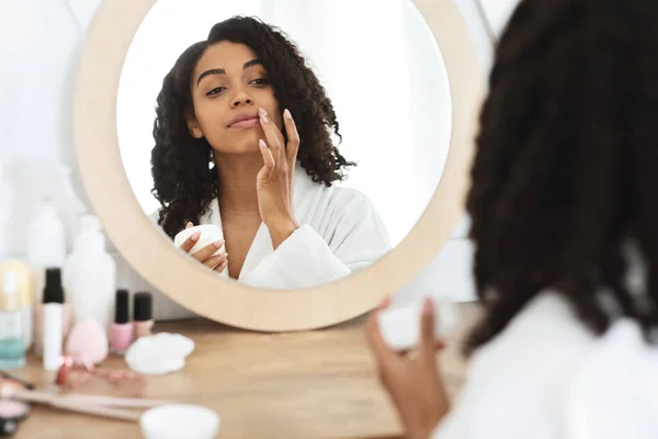 Уход за губами. Черная женщина, увлажняющая бальзам, отражается в зеркале — стоковое фото