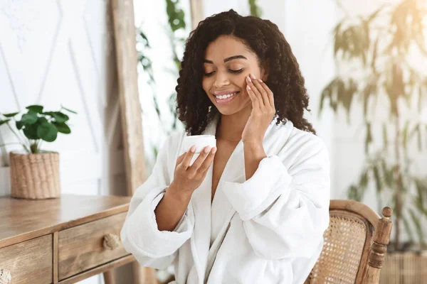 Huidhydratatie. mooie jonge vrouw in badjas aanbrengen crème op haar gezicht — Stockfoto
