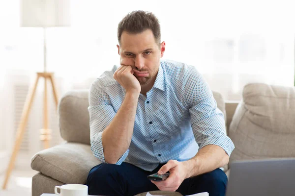 Tired man watching TV at home, holding remote control — Stock Photo, Image