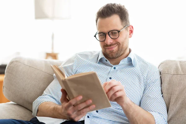 Hombre guapo en gafas leyendo un libro en casa — Foto de Stock