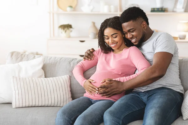 Прекрасные улыбающиеся будущие родители сидят дома на диване — стоковое фото