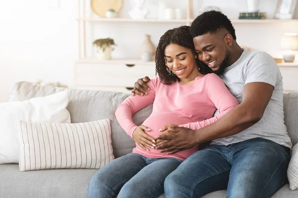 Schön lächelnde werdende Eltern sitzen zu Hause auf dem Sofa — Stockfoto