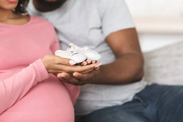 Closeup of baby footwear in black man and woman hands — Stock Photo, Image