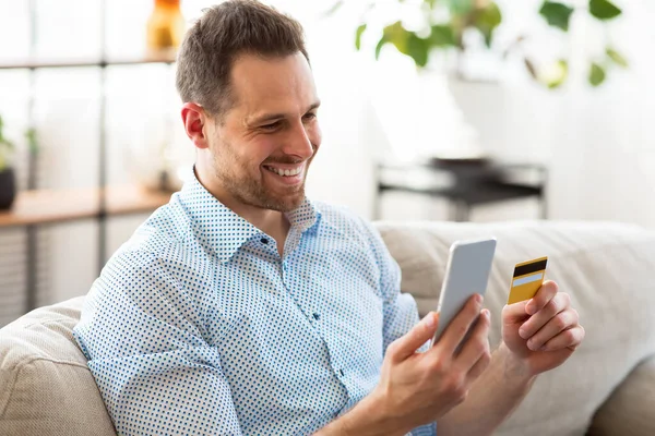 Hombre adulto alegre sosteniendo teléfono inteligente y tarjeta de crédito —  Fotos de Stock