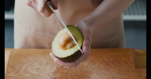 Жінка видаляє насіння авокадо з ножем на кухні — стокове відео