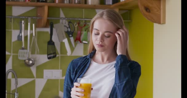 Jonge vrouw drinkt sinaasappelsap in de keuken — Stockvideo