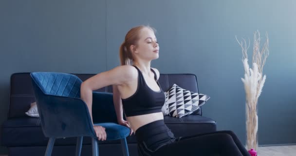 Mujer joven haciendo sentadillas apoyada en la silla, entrenando en casa — Vídeo de stock