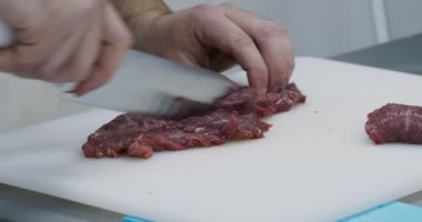 Profesyonel erkek aşçı mutfak masasında taze et kesiyor.