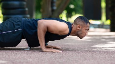 Açık havada çalışan kaslı siyahi adamın yan görüntüsü, parkta şınav çekerken.