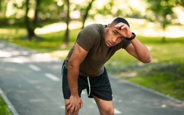 Atletik siyah adam şehir parkındaki sabah koşusundan sonra yorgun hissediyor.