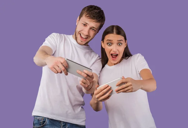 Aufgeregtes Paar benutzt Mobiltelefone auf lila Hintergrund — Stockfoto