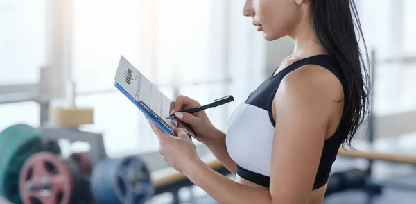 Personal trainer filling out workout planner at sports club, copy space — Stock Photo, Image